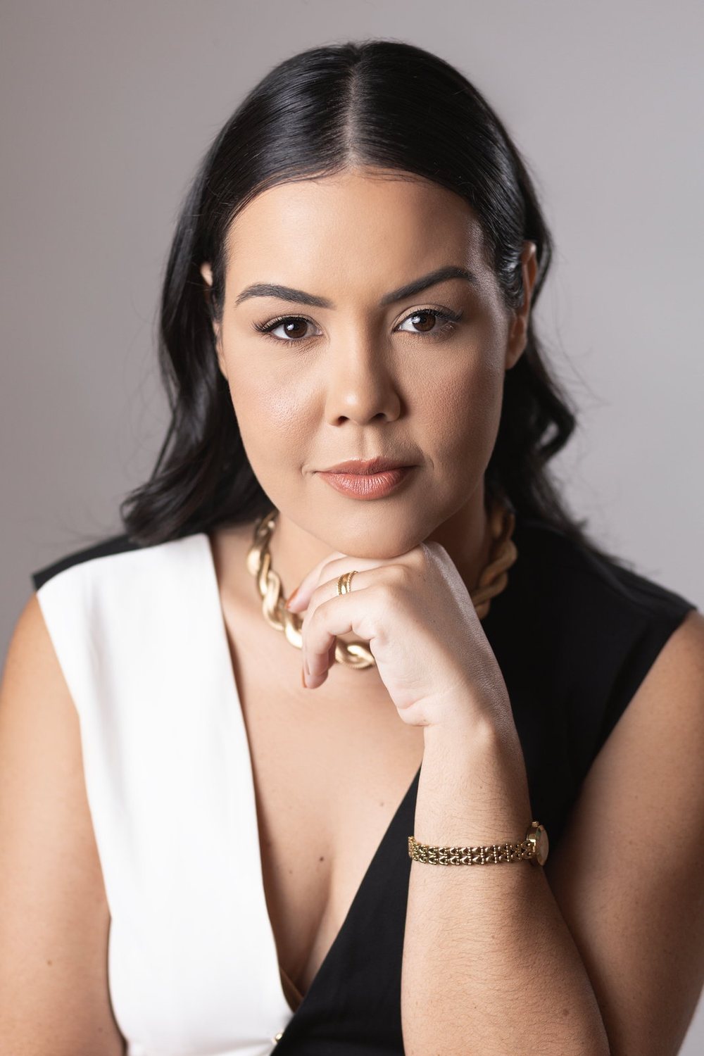 Jennedy Lima em retrato de estúdio, blazer preto e branco, a mão apoiada no queixo, olhando para a câmera.